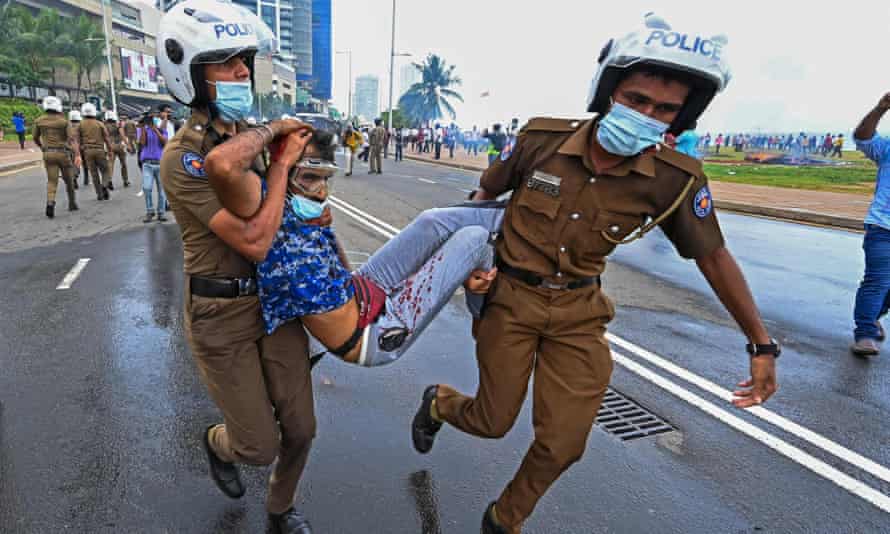 Police officers carry an injured man during a clash between government supporters and demonstrators in Colombo